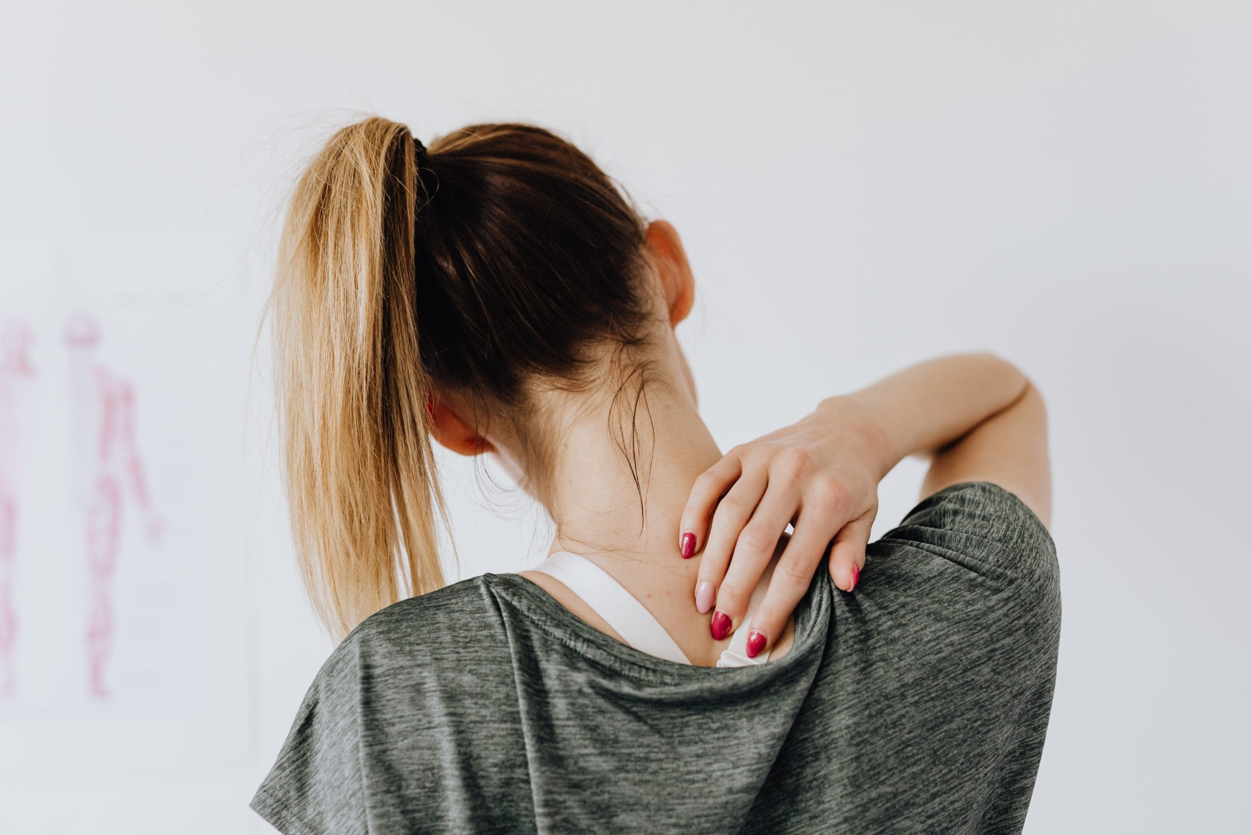 A woman with her back facing out, holding her neck in pain.