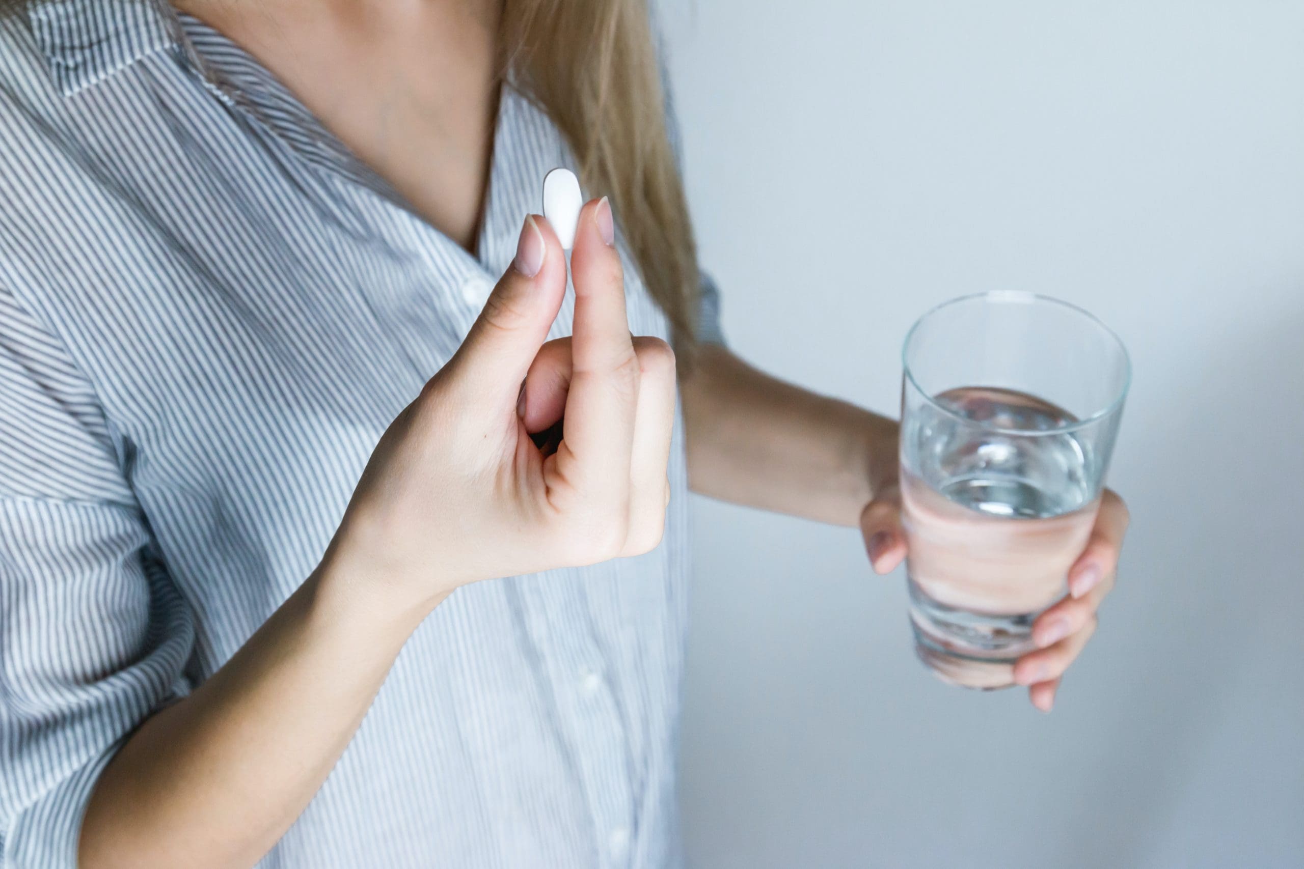 Woman holding a pill in one hand and a glass of water in another.